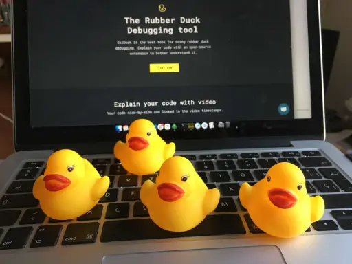 Cztery żółte gumowe kaczuszki siedzą na klawiaturze laptopa, obok ekranu z napisem "The Rubber Duck Debugging tool".