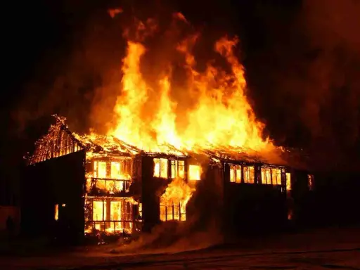 Une maison à deux étages est dévorée par les flammes, le toit s'effondre. L'incendie cause une destruction massive.