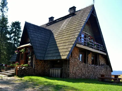 Drewniana bacówka na Turbaczu, z kamiennymi schodami i stosem drewna. Stare wierchy zapraszają do odpoczynku.