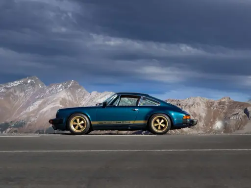 Ein türkisfarbener Porsche 911 SC mit goldenen Felgen und Streifen steht auf einer Bergstraße. Die Wertentwicklung dieses Klassikers ist beeindruckend.