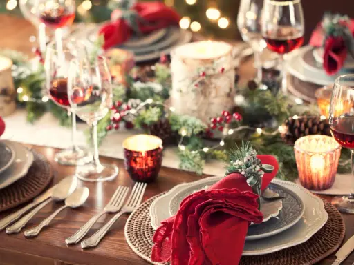 Tavola apparecchiata per un magico pranzo di Natale, con candele, pigne e luci scintillanti. Dove andare per un'atmosfera così?