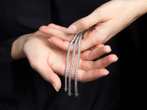 Mani delicate tengono tre scintillanti bracciali tennis, un classico intramontabile la cui storia affonda le radici nel mondo dello sport.