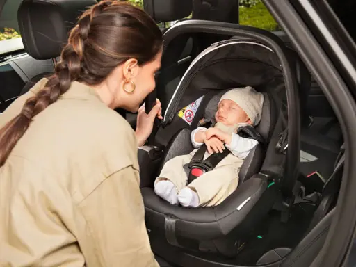 Madre mira a su bebé dormido en la silla coche, asegurando la correcta postura recien nacido silla coche para un viaje seguro.