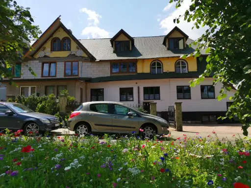 Willa pod zielonym wierchem, z kolorowym ogrodem i samochodami przed wejściem.