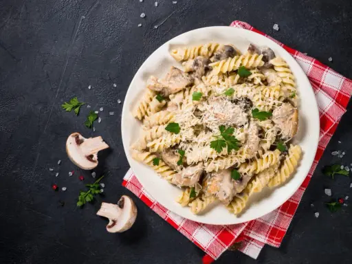 Pyszny makaron z kurczakiem i pieczarkami w kremowym sosie, posypany parmezanem i świeżą pietruszką.