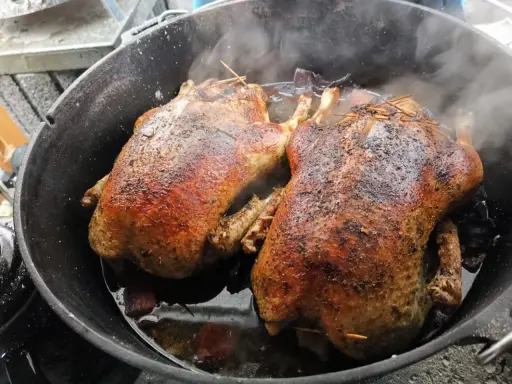 Zwei goldbraune Enten garen im Dutch Oven. Dampf steigt auf, während die Enten im eigenen Saft schmoren.