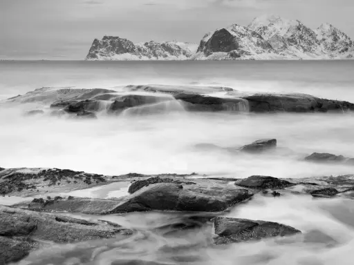 Vatten virvlar runt stenar vid en snötäckt kust. Perfekt för zoom fotoresor.