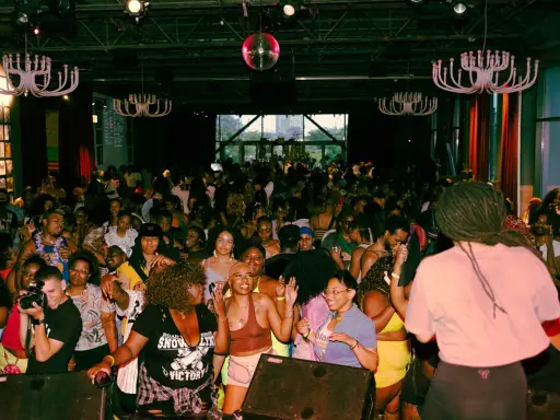 A vibrant crowd dances at a lively event, possibly one of the best gay bars in Chicago, under a disco ball and ornate chandeliers.
