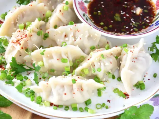 Pierożki gyoza, posypane szczypiorkiem i sezamem, podane z sosem.