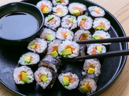 Un plato negro lleno de maki sushi de salmón y aguacate, listo para ser disfrutado con salsa de soja.