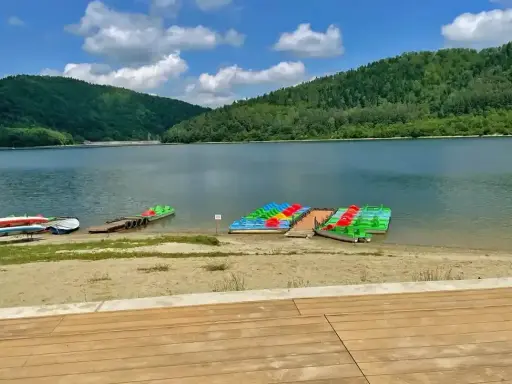 Jezioro Klimkowskie plaża z kolorowymi rowerami wodnymi i kajakami, otoczona zielonymi wzgórzami.