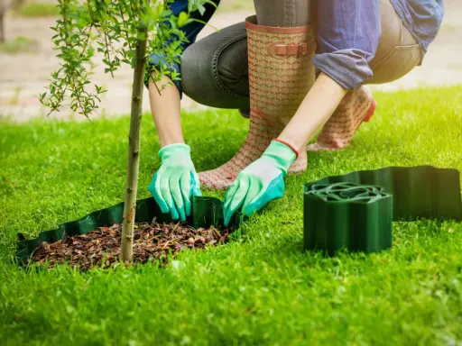 Osoba w zielonych rękawiczkach układa plastikowe obrzeża, by z nich zrobić obrzeża w ogrodzie.