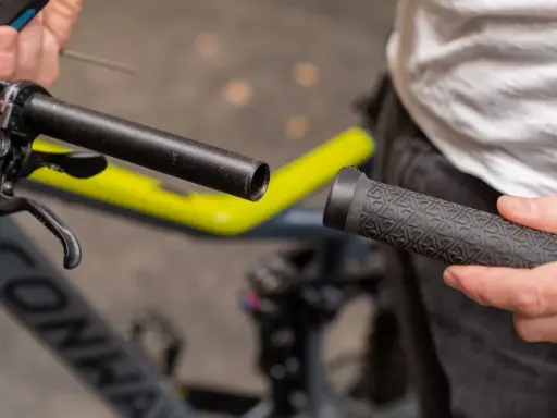 Person wechselt Fahrradgriffe. Der Lenker ist freigelegt, die neue Griff wird bereitgehalten.