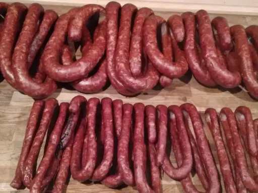 Dwie linie świeżej, swojskiej kiełbasy ułożone na drewnianym blacie. Idealne do wypróbowania przepisu na kiełbasę swojską.