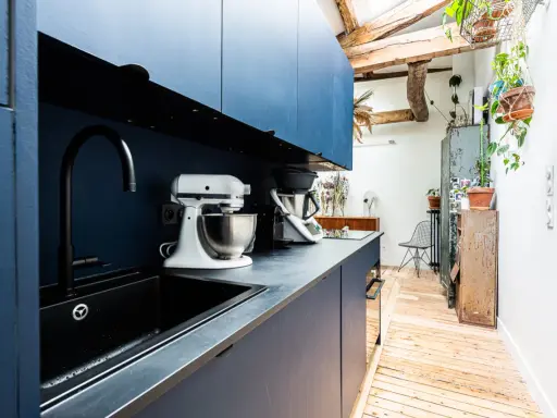 Cuisine moderne avec armoires bleues, évier noir et robot pâtissier. L'entrée de la maison donne directement dans cette pièce fonctionnelle et stylée.
