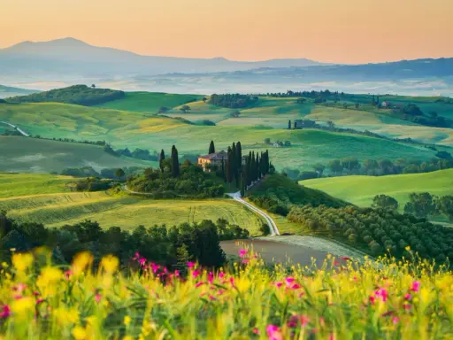 Un casale solitario su una collina, circondato da cipressi e dolci colline verdi, un sogno per un tour della Toscana.