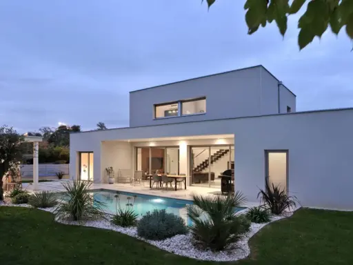 Vue arrière d'une maison moderne avec piscine illuminée, terrasse et jardin paysager. Un exemple de plan maison de luxe.