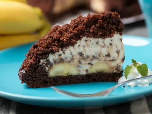 Ein Stück saftiger Maulwurfkuchen vom Blech mit Bananen und Schokostückchen in der Creme, garniert mit Sahne und Minze.