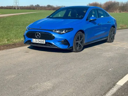 Blauer Mercedes-Benz CLA 250+ EQ auf einer Straße, mit grünen Feldern und einem Strommast im Hintergrund.