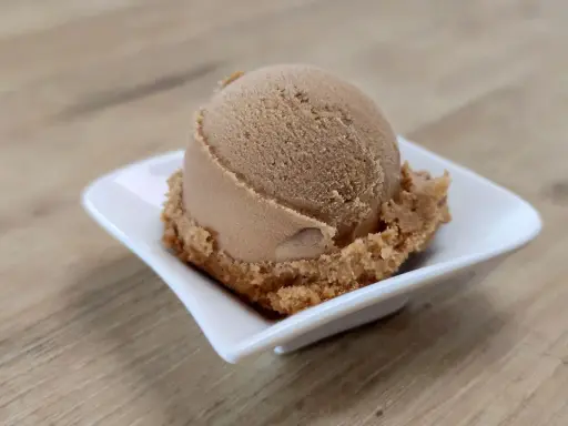 Eine Kugel cremiges Coca Cola Eis in einer weißen Schale auf Holzhintergrund.