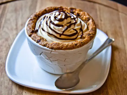 Un délicieux dessert dans une tasse en cookies, garni de crème fouettée et de sauce au chocolat.