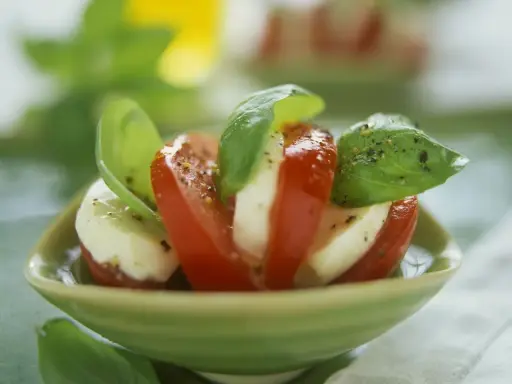 Tomate Mozzarella, ein gesundes Gericht, garniert mit frischem Basilikum und Pfeffer, serviert in einer grünen Schale.