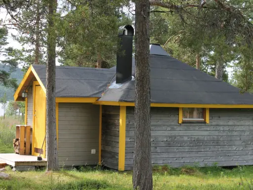 En mysig stuga för camping i Kiruna, omgiven av skog och med en sjö i bakgrunden.