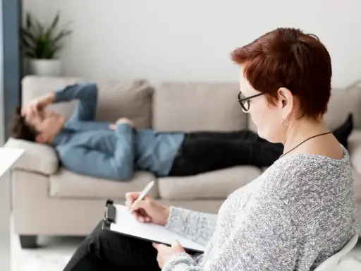 Terapia u psychologa. Mężczyzna leży na kanapie, zmagając się z problemami, które mogą być dda objawy. Terapeuta notuje.