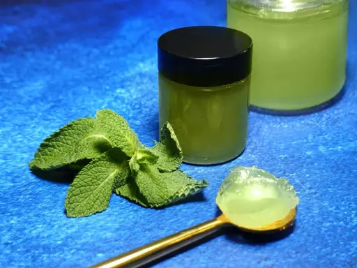 Une cuillère dorée présente une portion de gelée de menthe fraîche. À côté, un pot fermé et un autre ouvert contiennent cette même gelée verte et rafraîchissante.
