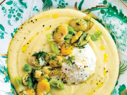Macco di fave fresche cremoso, guarnito con fave intere, ricotta fresca e aneto, servito su un piatto decorato.