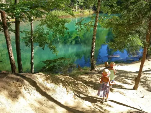 Dwie dziewczynki w słomkowych kapeluszach spacerują ścieżką nad turkusowym jeziorem. Idealne miejsce, gdzie w góry z dziećmi na Śląsku.