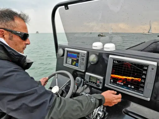 Un homme navigue, consultant un écran de sonar affichant des données sous-marines.