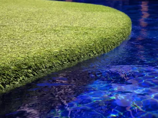 A vibrant green artificial grass island floats in a bright blue pool. The question of will chlorine kill grass is answered by this synthetic turf, unaffected by the water.