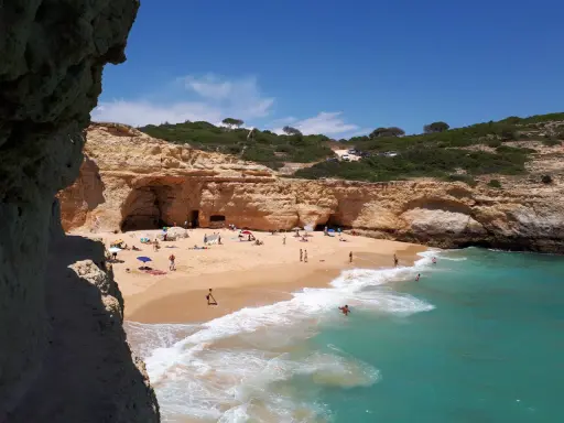 Sonniger Strand an der Algarve, ein echter Geheimtipp mit Felsformationen und türkisfarbenem Wasser. Menschen entspannen sich am Sandstrand.