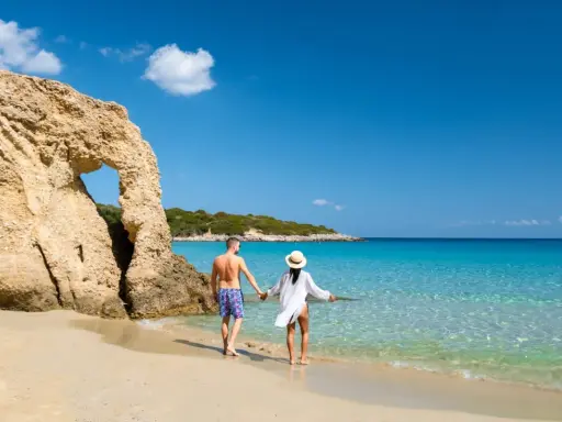 Para, trzymając się za ręce, spaceruje po piaszczystej plaży z turkusową wodą. Czy Cypr jest bezpieczny? Tak, to idealne miejsce na wakacje.