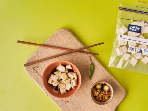 Vorbereitung für tofu einfrieren: gewürfelter Tofu in Schüssel mit Soße, daneben Stäbchen, Chili und ein Gefrierbeutel mit Tofuwürfeln.