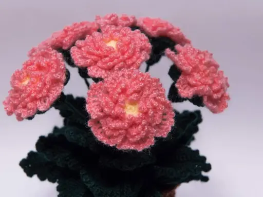 En bukett av virka blommor i rosa med gula mittar och mörkgröna blad.