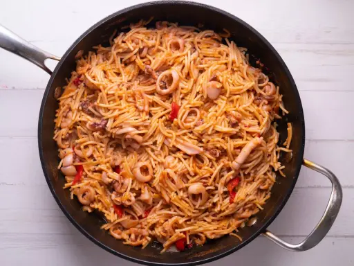 Fideuà de marisco en paellera, con fideos finos, calamares y pimientos rojos. ¡Perfecta para aprender como hacer fideuà!