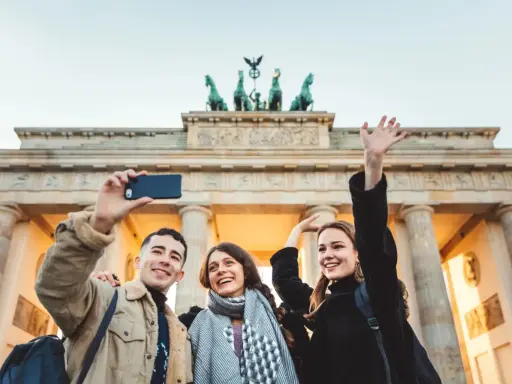 Tre glada vänner tar en selfie framför Brandenburger Tor, en ikonisk sevärdhet att se i Berlin.