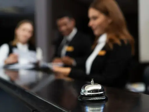 Dzwonek przy ladzie hotelowej, gdzie pracownicy obsługują gości. Stanowiska pracy w hotelu tętnią życiem.