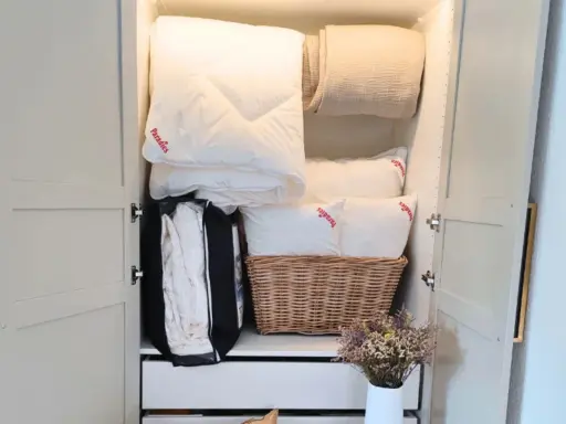 Ordentlich verstaut: weiße Bettdecke falten und Kissen im Schrank, daneben eine Decke und ein Korb mit Bettzeug.