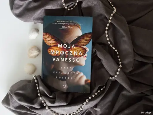 Okładka książki "Moja mroczna Vanesso" z motywem motyla na twarzy dziewczyny, otoczona szarym materiałem i koralikami.