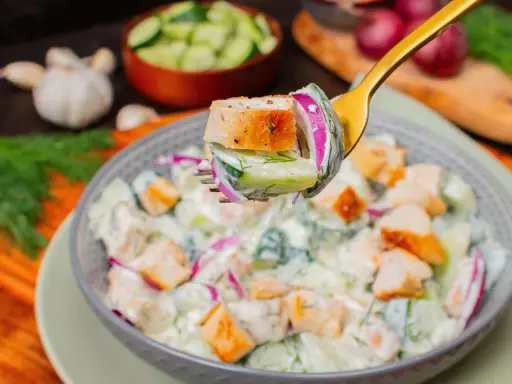 Ein Löffel mit einem Stück Hähnchen, Gurke und roter Zwiebel, bereit, in einen cremigen Salat zu tauchen. Perfekt für proteinreiche Salate!
