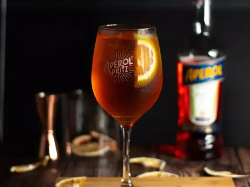 Orzeźwiający Aperol Spritz z plastrem pomarańczy, obok butelki Aperolu. Poznaj różne rodzaje Aperolu i jego zastosowania.