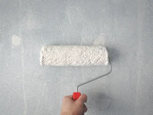Main tenant, comment rattraper une peinture mal faite. Un rouleau à peinture blanc est tenu par une main sur un mur bleu clair texturé.
