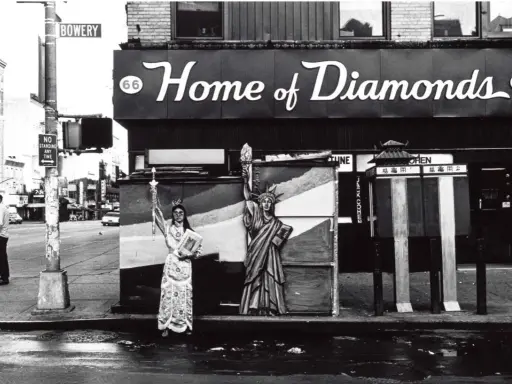 Corky Lee photos: A person in ornate robes stands beside a Statue of Liberty cutout on a wet street, with "Home of Diamonds" sign above.