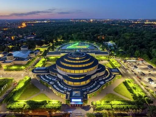 Wrocław Hala Stulecia nocą, z podświetloną fontanną i otaczającym parkiem.