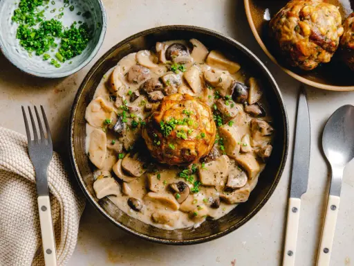 Herzhaftes Gericht: Ein Knödel in cremiger Pilzrahmsoße, garniert mit Schnittlauch. Perfekt, was passt zu Brezenknödel!