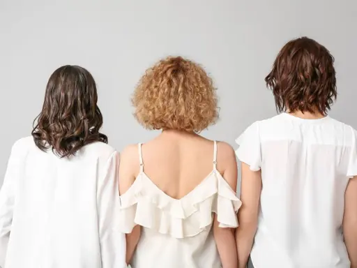 Trzy kobiety z tyłu. Jedna ma falowane, ciemne włosy, druga krótkie, kręcone blond włosy w stylu boho, trzecia falowane, brązowe włosy.