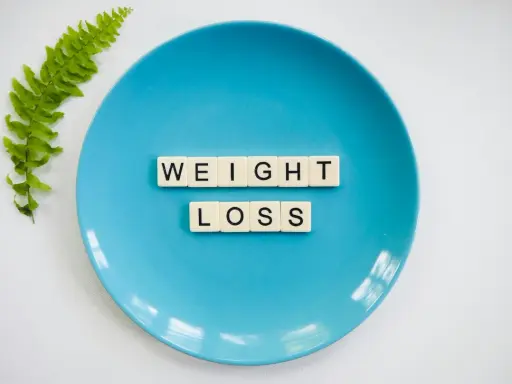Niebieski talerz z literami tworzącymi napis "WEIGHT LOSS" i gałązką paproci. Pytanie o makro na redukcji?